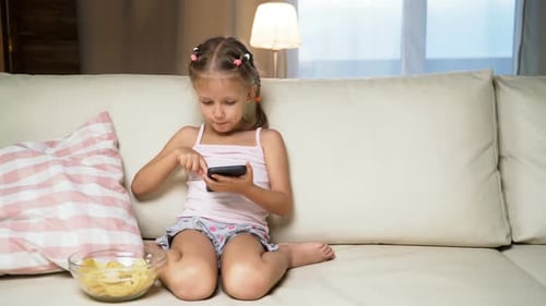 Girl Uses Mobile Phone on Couch with Chips