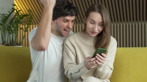 Young Couple Reacts to Phone on Yellow Couch