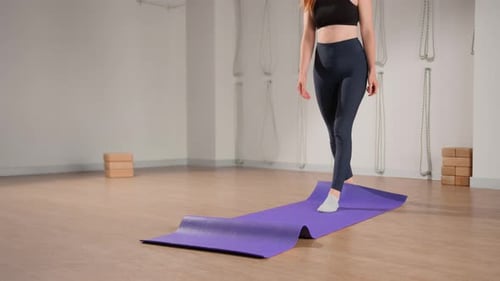 Woman rolling up yoga mat after training in studio. Girl folding fitness mat on floor at yoga studio