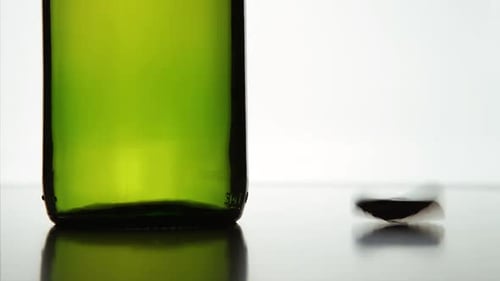 The cap falls near a green bottle. White background