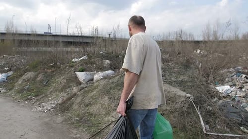 Man Walking Through Polluted Area with Trash Bags