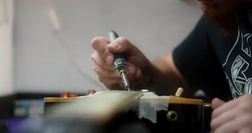 Luthier calienta los trastes de la guitarra soldando el hierro antes de refrescar los preparativos del artesano de la guitarra para