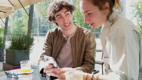 Young couple talking excitedly over smartphone, sitting in cafe