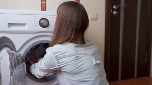 Woman Loads Laundry Into Washing Machine in Home