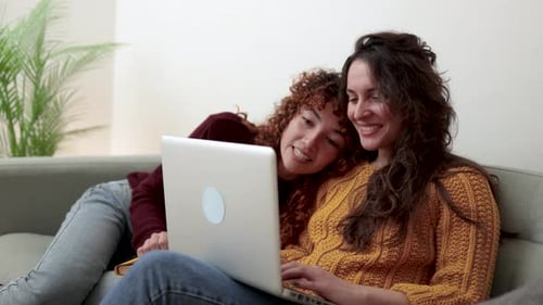 Hispanisches lesbisches LGBT-Paar benutzt Computer-Laptop im heimischen Wohnzimmer Homosexuelle Liebesbeziehungen