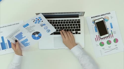 Geschäftsfrau tippt auf Laptop-Tastatur mit Finanzdiagrammen auf dem Tisch