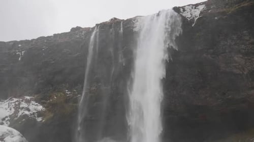 Dramatic Waterfall Flowing Over Snowy Rocky Cliff