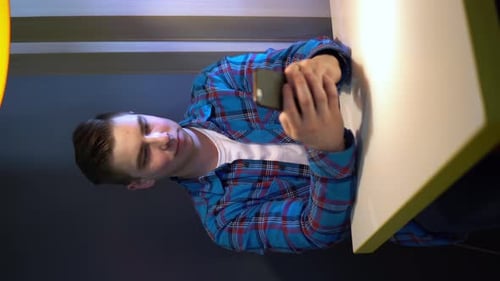 A Young Man with a Phone Sits at a Table. A Man Sits at Cafe at a Table with a Smartphone and Is in