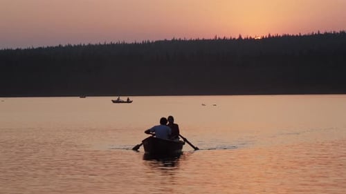 Romantic Couple Rowing Boat on Lake at Sunset