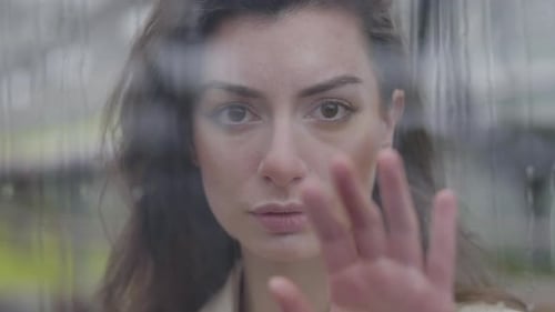 Nahaufnahme einer jungen kaukasischen Frau, die hinter Glas steht und das Fenster mit der Hand berührt. Portrait von