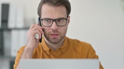 Close Up of Young Man with Laptop Talking on Smartphone