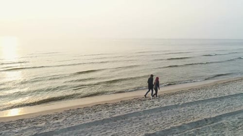 Couple Walks Along Beautiful Sandy Beach at Sunset