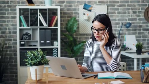 Female Office Worker Talking on Mobile Phone and Using Laptop Then Taking Notes