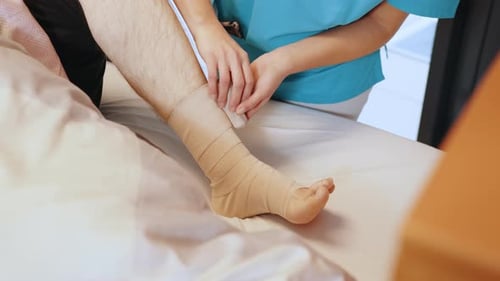Closeup of Male Doctor Bandaging Foot of Female Patient at Doctor's Office