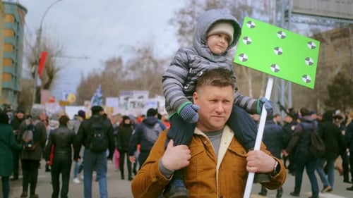 Father Carries Son Through Urban Crowd With Sign