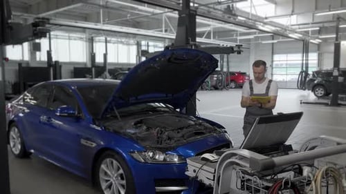 Mature Male Mechanic Making Notes and Using Computer While Repairing a Car