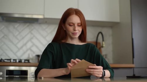 Woman Opening Letter at Kitchen Table