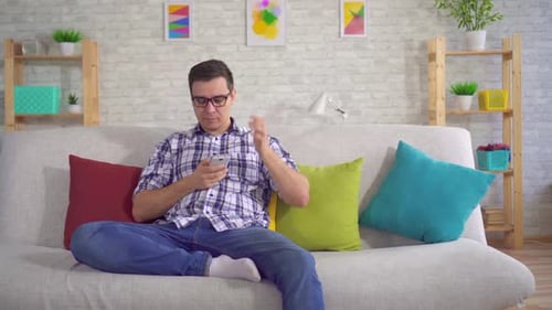 Man Relaxing on Couch, Using Smartphone