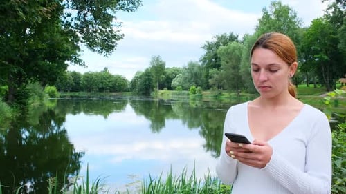 Young Woman Uses Phone and Smiles in the Park.
