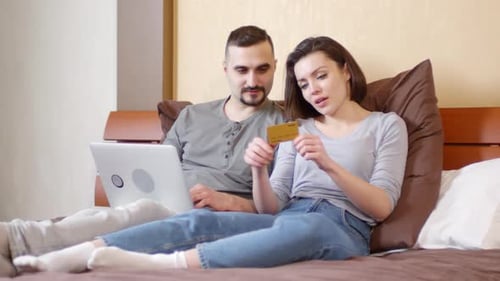 Couple Shopping Online with Credit Card on Bed