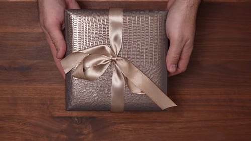 Present Held in Hands on Wooden Table