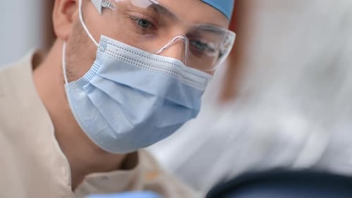 Estomatologista de closeup com óculos de proteção e máscara facial médica trabalhando com o paciente na clínica