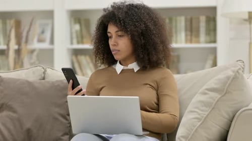 Woman Uses Laptop and Phone on Couch at Home