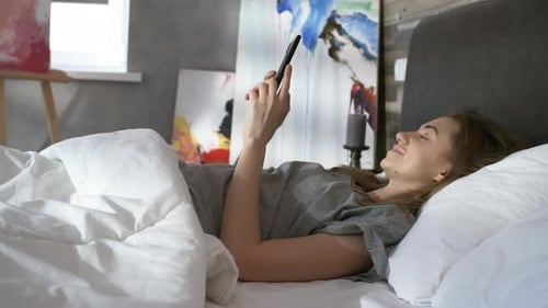 Woman Lying in Bed Using Cell Phone