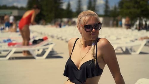 Close-up, Travelling: Blonde Girl Is Sitting on Deck Chair, on Beach, in Sunglasses