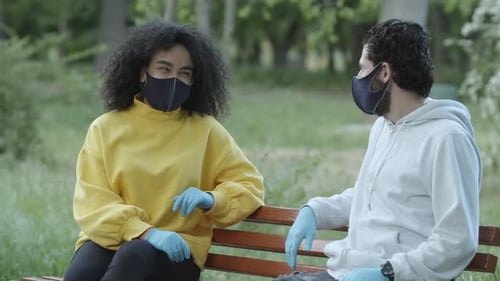 Man and Woman Talking on Park Bench With Masks
