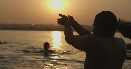 Hindu man praying at sunrise in Ganga river in Varanasi, India