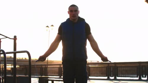 Young Sportive Man Jumping Over the Rope on Sunset