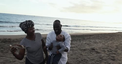 African parents and cute little son having fun on the beach at sunset