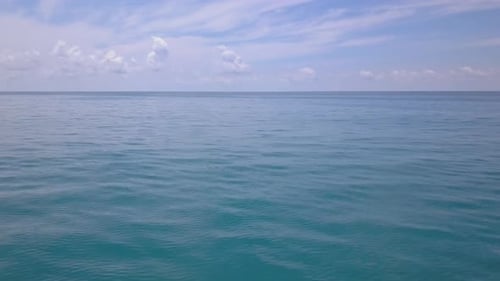 Luftaufnahme fliegt über türkisfarbene Meereswellen, Drohnenkamera bewegt sich langsam tief über der blauen Wasseroberfläche