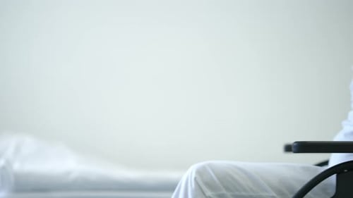 White Bed in Hospital Ward with Unrecognizable Caucasian Man Rolling Wheelchair Entering