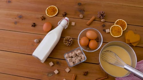 Olla con ponche de huevo, ingredientes y especias sobre madera