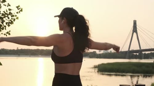 Woman Stretching Arms Beside River at Sunrise