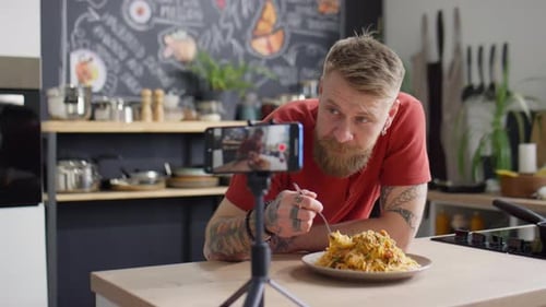 Tattooed Man Enjoys Spaghetti While Vlogging in Kitchen