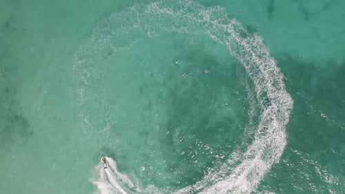 Aerial top view of jet ski or boat drawing a shape on sea ocean turquoise water. Adventure