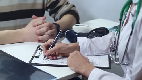 Doctor Writes on Medical Chart During Patient Consultation