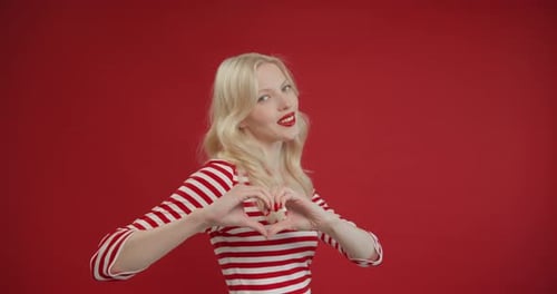 Closeup Smiling Young Woman Making Sign Heart Shape By Hand Posing at Red Studio Background