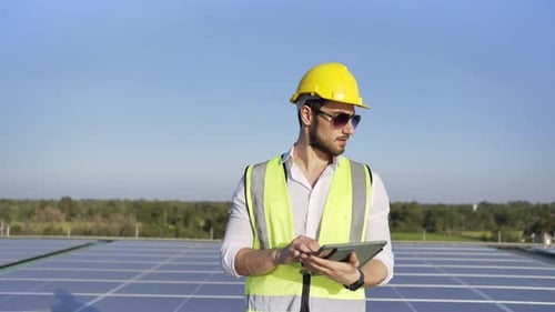 4K Professional man engineer using digital tablet maintaining solar cell panels on building rooftop.