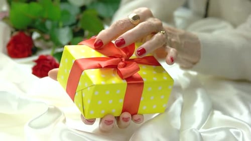 Senior Woman Untying a Birthday Gift with Red Bow