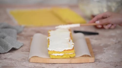 Nahaufnahme von Frauenhänden, die süßen Biskuitkuchen mit weißer Sahne und Aprikosenmarmelade backen