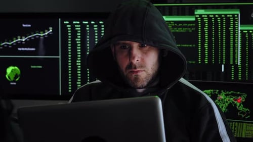 Porträt eines kriminellen Hackers mit Kapuze, der am Schreibtisch sitzt und in Regierungsdaten oder große Unternehmensdaten einbricht