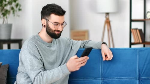 Man Relaxing on Couch Using Mobile Phone