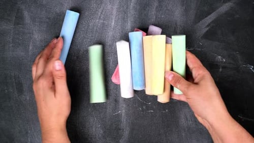 female hand puts a stack of colored crayons for drawing on a black surface, top view