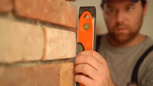 Man Checks Brick Wall with Leveling Tool