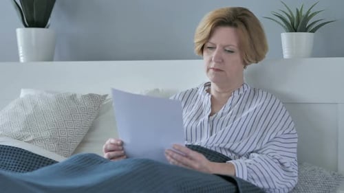 Mature Woman Reads Documents in Bed at Home