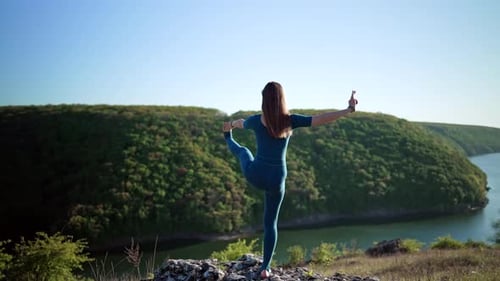 Woman in Blue Overalls Practicing Yoga Utthita Hasta Padangushthasana on High Cliff Above Water